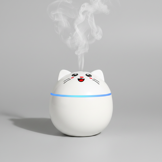 A white cat-shaped humidifier or diffuser with a smiling face and whiskers, emitting a plume of steam from the top. It has a glowing blue light band around its middle and is photographed on a clean, light gray background.