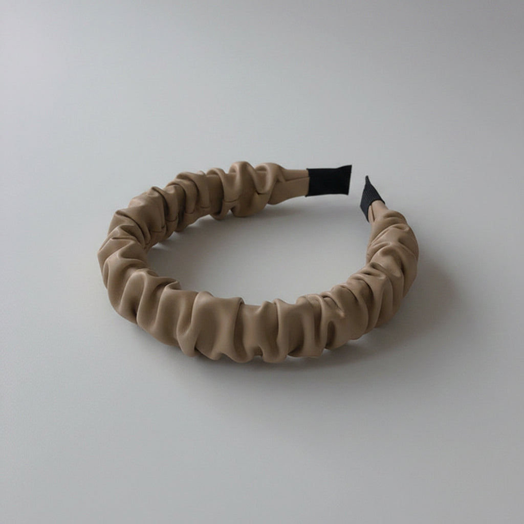 Beige headband on a white surface with a wooden coaster in the background