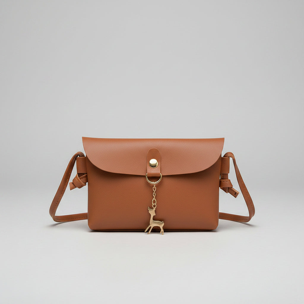 Brown leather handbag held by a person with a gold charm, on a tiled floor.