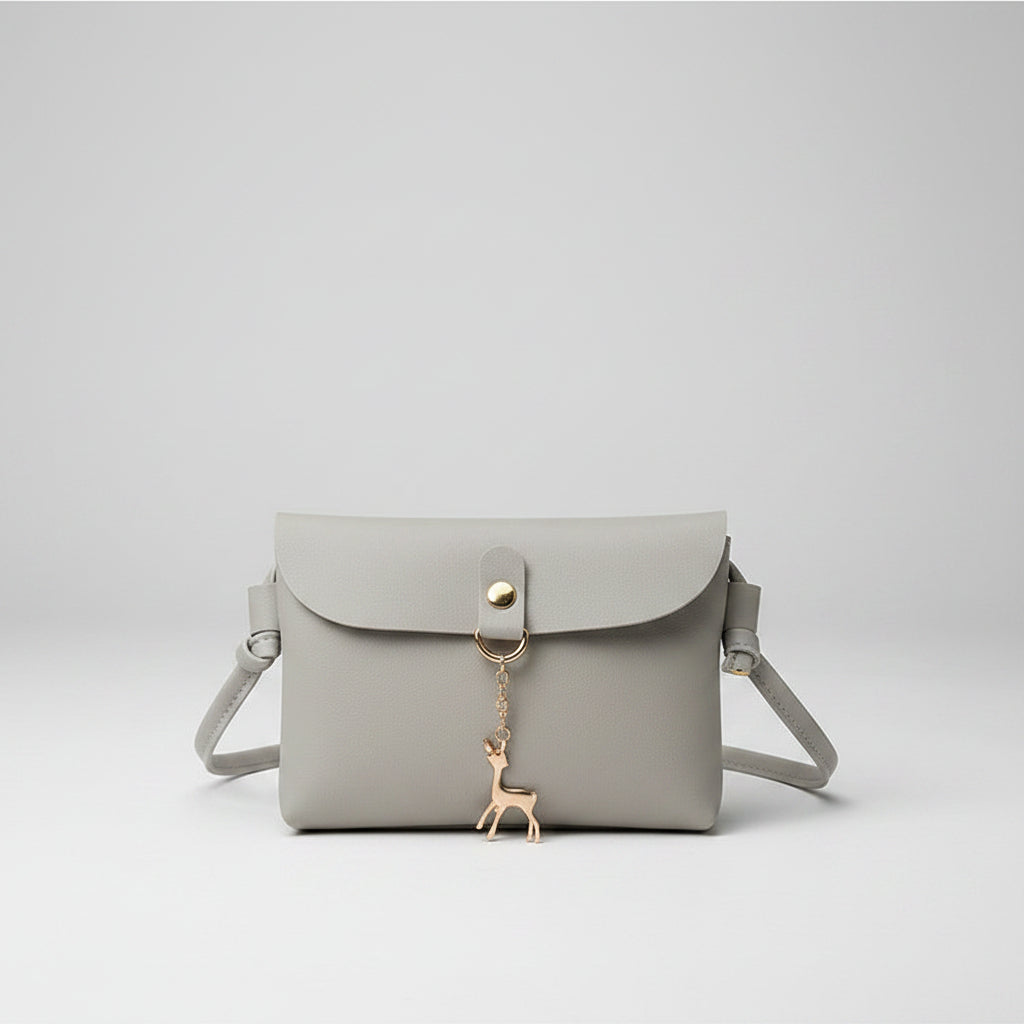 Light gray handbag with a gold chain and keychain held by a hand on top of a magazine.