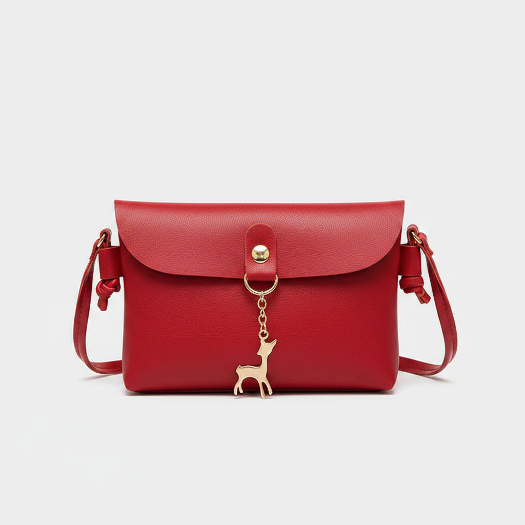 Red handbag with a gold charm held by a person on a gray floor.