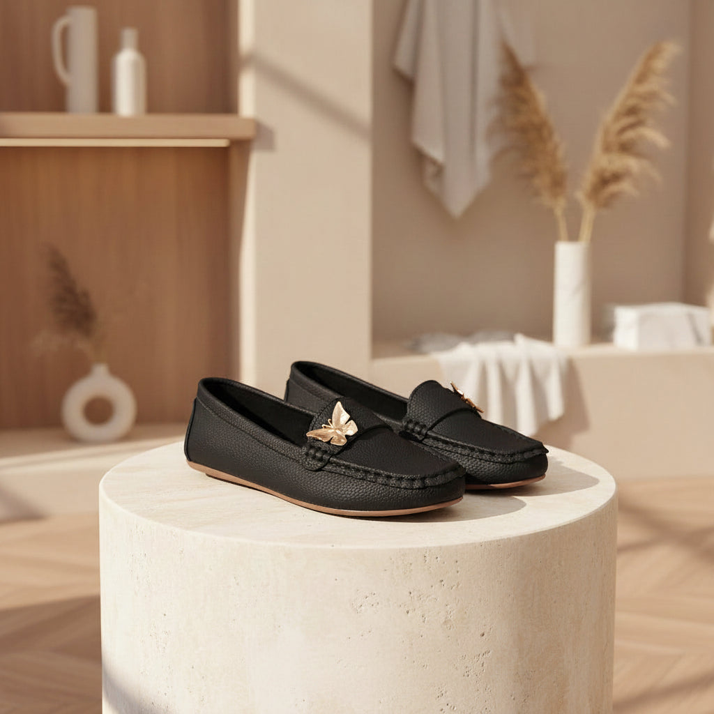 Black loafers with gold butterfly accents on a light wooden surface.