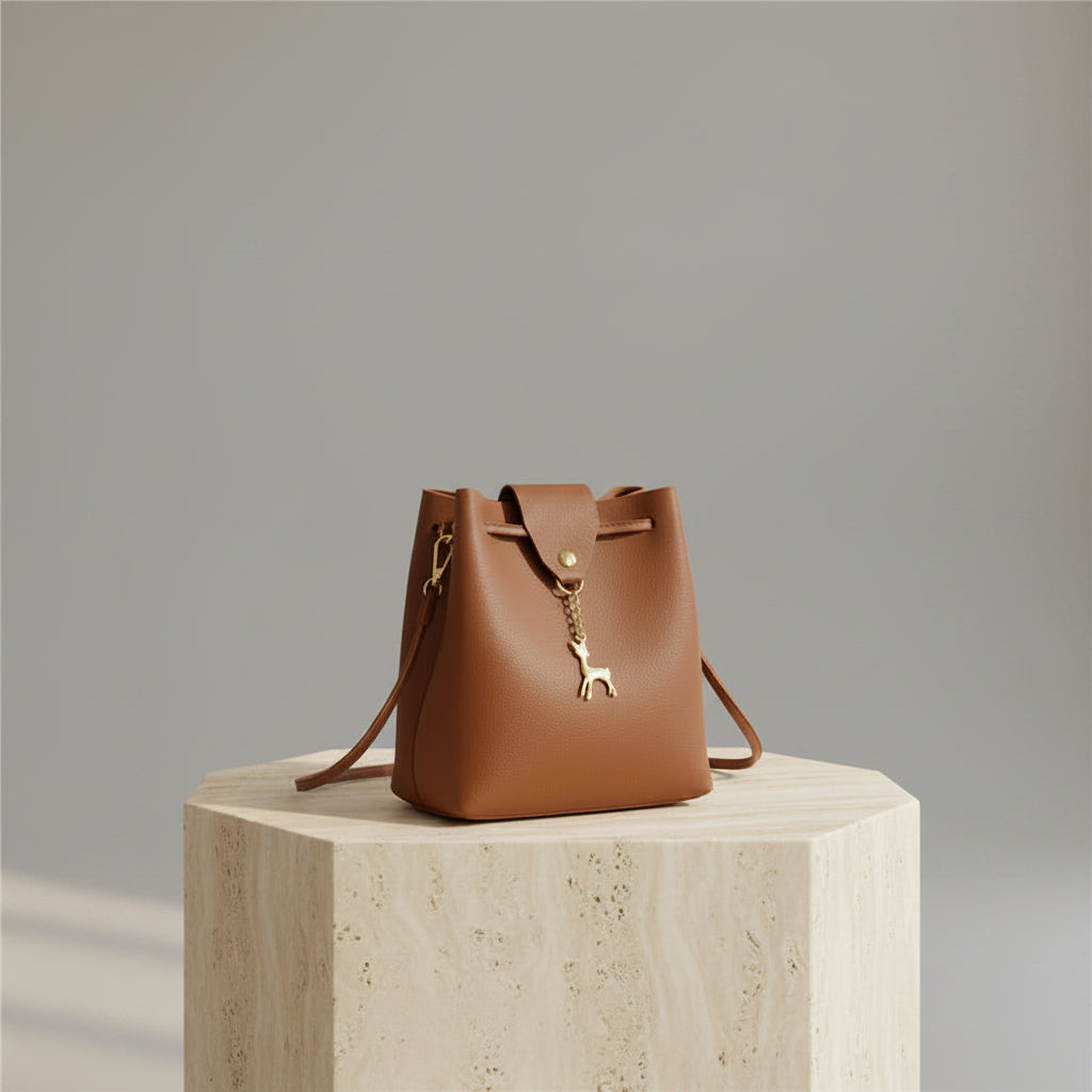 Brown handbag with a gold deer charm on a white surface